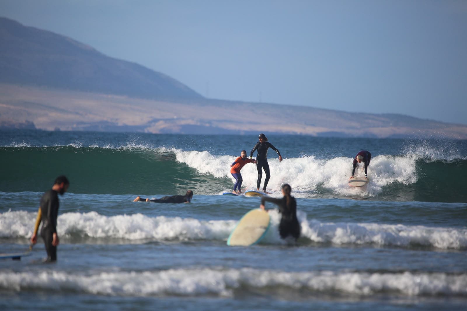 Several surfers riding the same wave together with a headland in the distance